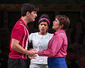 As You Like It, Shakespeare Theatre Company, Wedding Orlando in his red with stripes polo shirt and Orlando as Ganymede sans jacket hold both hands as the face each other. In the back is Celia in a simple gray patterned blouse.